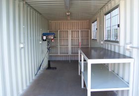 inside a shipping container workshop with benches and shelving.